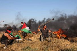 متظاهر فلسطيني يستخدم مقلاعًا لإلقاء الحجارة على الجنود الإسرائيليين خلال مسيرة بالقرب من السياج الحدودي