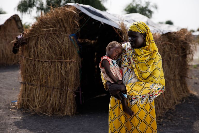سودانية تحمل ابنتها خارج ملجأها في مخيم للنازحين