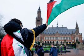 متظاهر يلوّح بالعلم الفلسطيني أمام مبنى محكمة العدل الدولية (رويترز)