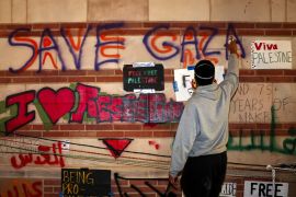 متظاهر يدعم الفلسطينيين في غزة يكتب عبارات تضامنية على أحد الجدران في جامعة كاليفورنيا (رويترز)