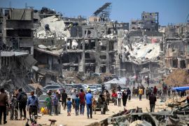أشخاص يمرون بجوار المباني المدمرة على طول أحد شوارع خان يونس بجنوب قطاع غزة (الفرنسية)